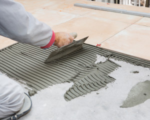 Home improvement, renovation - handyman laying tile, trowel with mortar